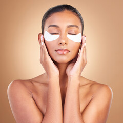 Skincare, eye patch and touch with Indian woman in studio for facial, spa treatment and glow. Self care, cosmetics and hydration with female model on brown background for mask, product and youth