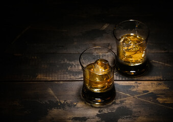 Luxury whiskey glasses with ice cubes on wooden background.