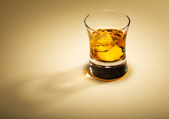 Single malt whiskey glass with ice cubes on golden background.