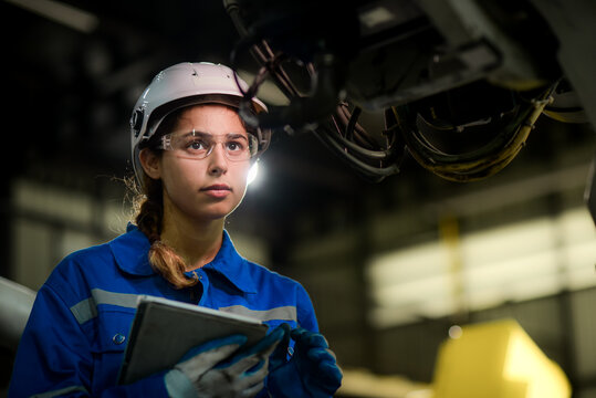 Caucasian female engineer, technician wearing safety uniform working use tablet Online information to monitor machine operation, check  maintenance plan to make a machine work efficiently and safely.
