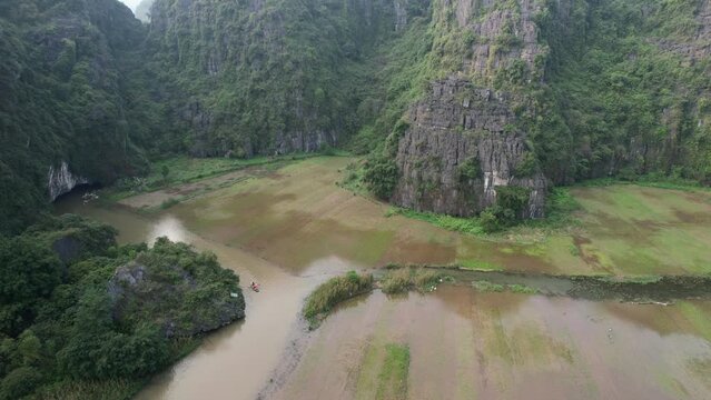 Flooded Rice Fields On The Riverbanks of Ngo Dong River in Ninh Binh Vietnam, People Cruising on Boats In Limestone Mountain Gorge - Drone View