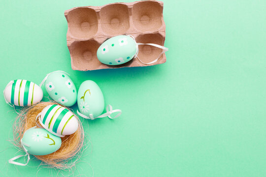 colorful handmade painted eggs in the nest and cardboard box on green background