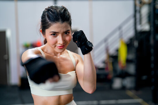 Portrait of Asian woman action of puch and hit also look at camera with smiling in fitness gym.