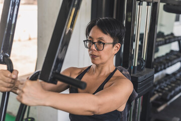 Fototapeta na wymiar A short haired asian woman does a set of chest flys on a pec deck machine at the gym. Targeting the pectoralis muscles