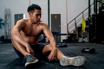 Obraz premium Front view of Asian sport man with shirtless sit on floor of fitness gym after finish of exercise.
