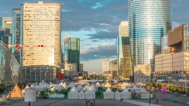 Modern skyscrapers during sunset timelapse in financial and business district of Paris - La Defense. Reflections on a glass with moving shasows at summer day. Arc de triomphe visible on the horizon.