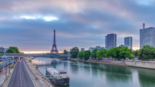 Eiffel Tower colorful sunrise timelapse with boats on Seine river and in Paris, France. Aerial view from Grenelle bridge. Modern buildings and traffic on a road. Dramatic clouds
