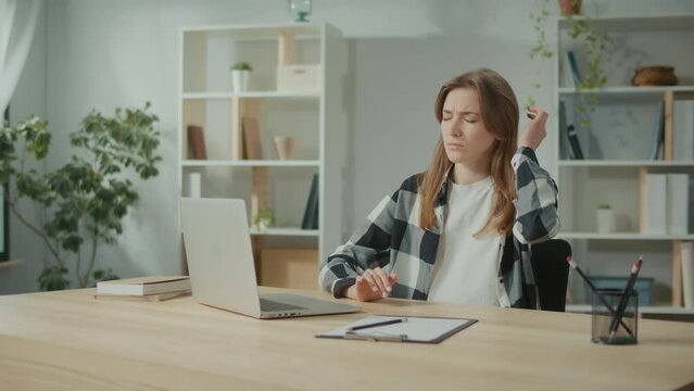 Focused Woman Work at a Table With a Laptop Suddenly Feeling Have Headache. Woman Feeling Tired of Long Sedentary Lifestyle. Try to Relax and Relieve Pain by Massages Her Head. Office Syndrome.