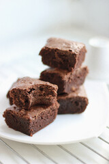 Close-up homemade chocolate brownies stacked on a white plate, side and top view. 