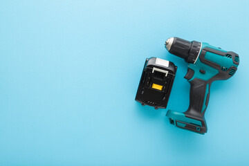 Cordless dark black green professional screwdriver with battery on light blue table background. Pastel color. Closeup. Tool for repair work. Top down view. Empty place for text.