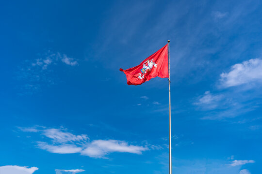 The historic flag of Lithuania, a rider with a sword on a white horse on a red background flutters against a bright blue sky with white clouds