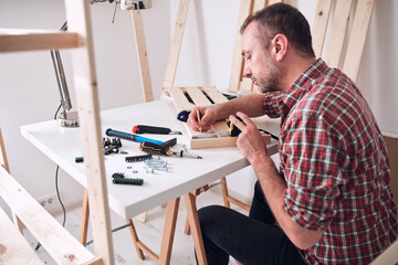 Obraz premium Man assembling new wooden shelf and furniture in the apartment.