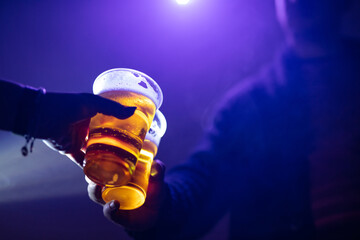 Man and woman cheering with a plastic cup of beer in the nightclub.