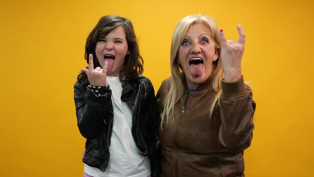video of grandmother and granddaughter sticking out their tongues and gesticulating standing on yellow background.