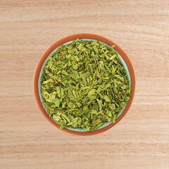 Overhead view of cut tarragon in a small terracotta bowl on a wood tabletop.