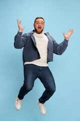 Handsome jumping man wearing white t-short spreading hands and smiling at camera over blue...