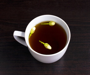 Jasmine tea. Cup of hot herbal tea with jasmine fresh flowers on a black table.