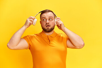 One confused man hears strange noise with surprised facial expression over yellow background