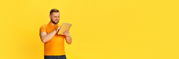 Banner with one handsome man using digital tablet and smiling with enjoying face isolated over yellow background. Copy space for ad