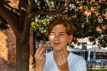Teenage boy doing italian hand gestures while standing under a tree
