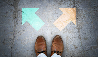Brown leather shoes and two colorful chalky arrows on asphalt - choice concept