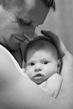 Happy father gently holds a newborn baby in his arms. The child looks into the lens. Father's day concept.  Black and white photography. Lifestyle documentary moment. Vertical photo.