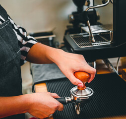Barista holding portafilter and coffee tamper making an espresso coffee in cafe