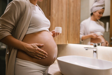 Close up of a pregnant woman applying anti-stretchmarks creme on her belly in the bathroom.