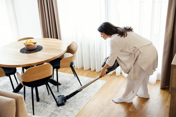 A woman is vacuuming under the kitchen table at home.