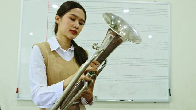 Portrait asian female student learning interested holding in the baritone instrument is practicing but doesn't know how to blow and press the notes making her confused how to use it.