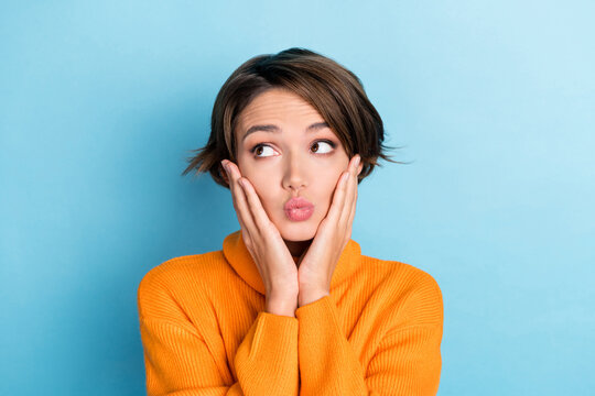 Portrait of adorable minded girl hands touch cheeks pouted lips look empty space isolated on blue color background