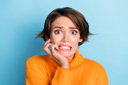 Photo portrait of lovely young lady bite fingers frightened terrible news dressed stylish orange outfit isolated on blue color background