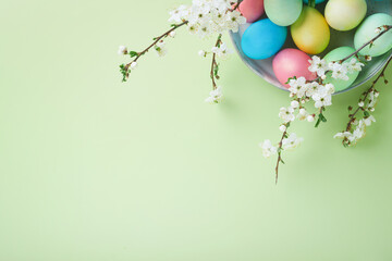 Happy Easter. Dyed Easter eggs on rustic table with cherry blossom tree branch on green background. Easter holiday card background with copy space. Top view.