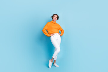 Obraz na płótnie Canvas Full length photo of lovely young lady hands waist posing shopping banner dressed stylish orange garment isolated on blue color background