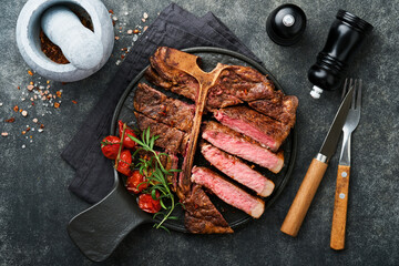 Steaks T-bone. Sliced beef grilled T-bone or porterhouse meat steak with spices rosemary and pepper on black marble board on old wooden background. Top view. Mock up.