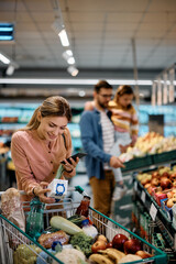 Happy woman reads nutrition label on milk pack while shopping in supermarket.