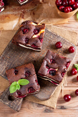 Chocolate brownie with cherries and cheese layer. Many pieces of chocolate dessert on a wooden board