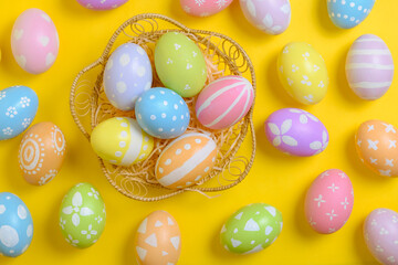 Happy easter celebration holiday. colourful pastel painted eggs in wicker basket nest decoration on a yellow background. Seasonal greeting gift card concept. Top view, flat lay, copy space.