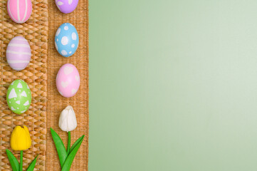Happy Easter holiday greeting card design concept. Colorful Easter Eggs and spring flowers on pastel green background. Flat lay, top view, copy space.