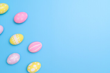 Happy Easter holiday greeting card design concept. Colorful Easter Eggs and spring flowers on blue background. Flat lay, top view, copy space.