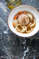 Escudella with pasta and pilota served in a beige soup bowl, vertical shot on a black marble background with space, high angle view
