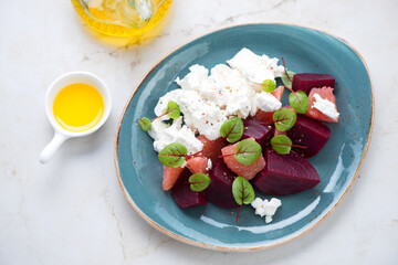Turquoise plate with beetroot, grapefruit and feta cheese salad, elevated view on a light-beige marble background, horizontal shot
