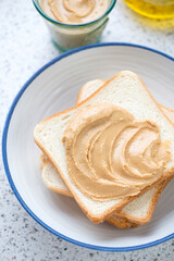 White plate with peanut butter sandwiches, vertical shot on a light-grey granite background, middle close-up, elevated view