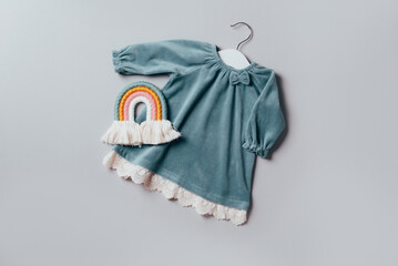 Blue dress for baby girl with white hanger, rainbow toy on grey background. Set of baby clothes and accessories for birthday party. Fashion childs outfit. Flat lay, top view. Copy space. Banner