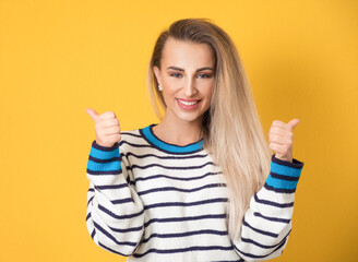 Young woman with thumbs up, like concept, isolated on yellow background. Yes gesturing, sings of good work