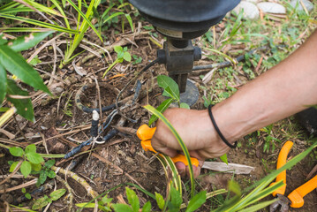 An electrician safely handles a faulty wire of a garden lamp with pliers. Electrical repair service at the garden of a house.