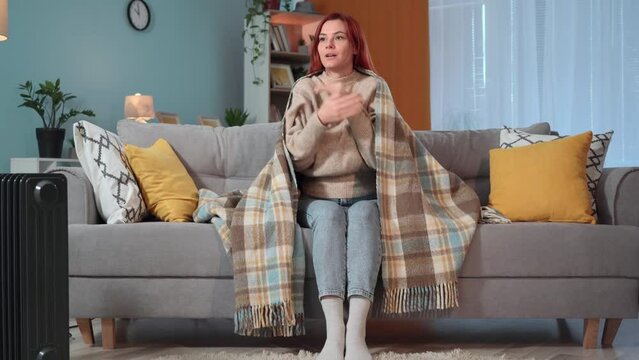 young woman is freezing at home due to lack of heating or non-payment of debts for utilities, housewife is warming herself under warm blanket sitting on sofa at home