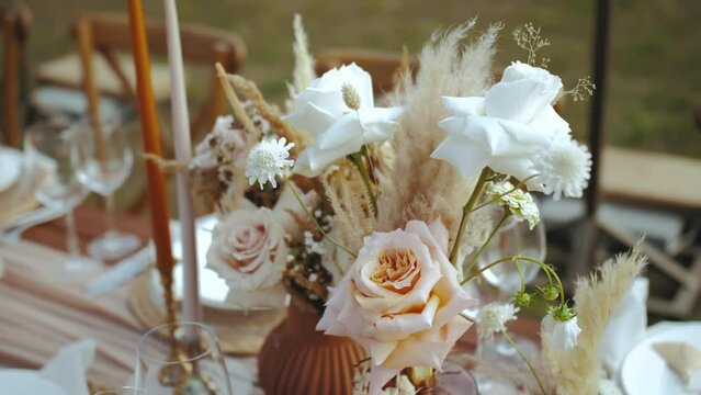 Close-up beautiful bouquet of roses and dried flowers on the table served and decorated with candles in boho style wedding dinner, plates and wine glasses, no people shot.