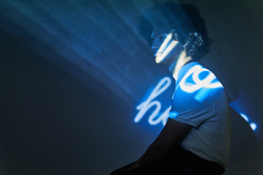 Young ethnic man in dark studio with blue text from projector