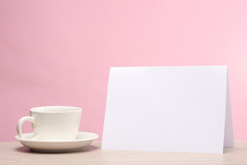 Fototapeta na wymiar Coffee cup with blank white paper calendar or table flyer mockup on pink background